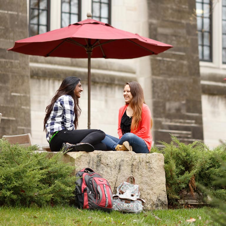 two female students talking under a red umbrella